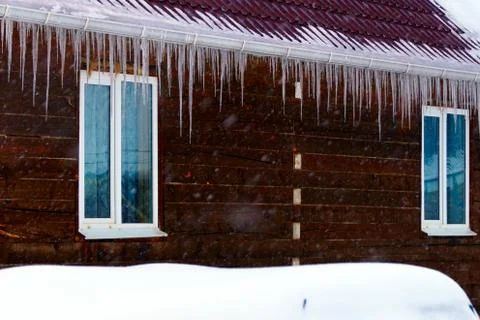 Many large and sharp icicles hang on the roof of the house. Stock Photos