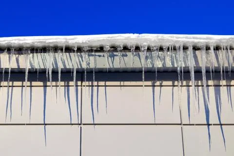Many large and sharp icicles hang on the roof of the house. Stock Photos