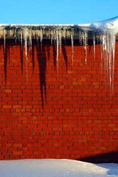 Many large and sharp icicles hang on the roof of the house. Stock Photos