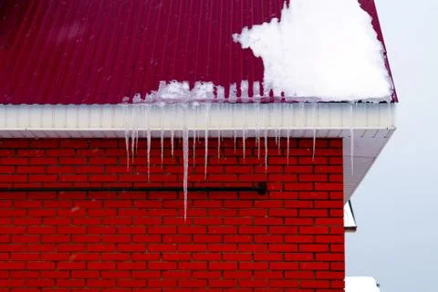 Many large and sharp icicles hang on the roof of the house. Stock Photos