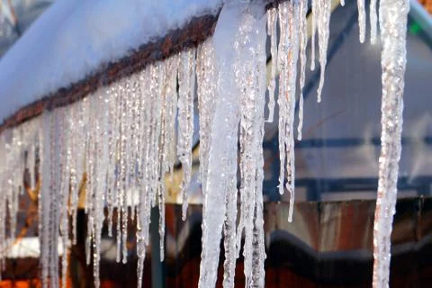 Many large and sharp icicles hang on the roof of the house. Stock Photos