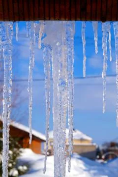 Many large and sharp icicles hang on the roof of the house. Stock Photos