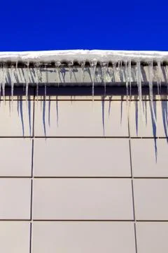 Many large and sharp icicles hang on the roof of the house. Stock Photos