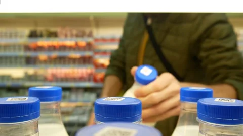Many milk bottles with blue caps on a supermarket shelf and a man takes one Stock Footage