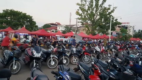 Many motorbikes parked in rows next to night market, people walk, Vientiane Stockbeeldmateriaal 80671845