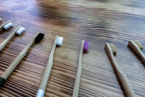Many multi-colored bamboo toothbrushes lie on a wooden background. Stock Photos