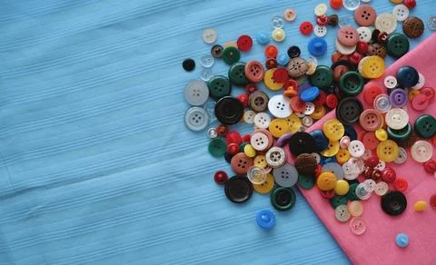 Many multi-colored buttons on blue fabric. Tailoring Stock Photos