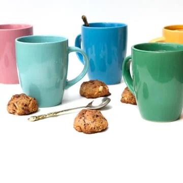 Many multi-colored mugs of lemon tea and homemade cookies on a white table. 스톡 사진