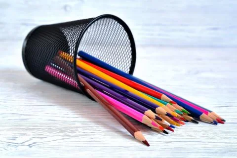 Many multi-colored pencils in a mesh glass on a light natural non-uniform bac Stock Photos