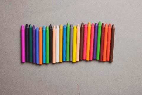 Many multi-colored wax crayons on grey paper. Flat lay Stock Photos