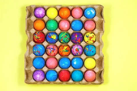 Many multicolored easter eggs in egg carton box on yellow background top view Stock Photos