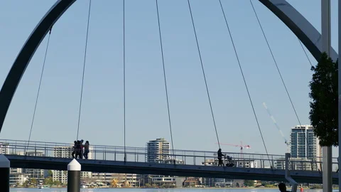 Many pedestrians cross single span suspension bridge over river Stock Footage 204055285