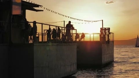 Many people on the pier enjoying orange sunset. Silhouettes of people against Stock Footage 211664751