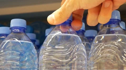 Many plastic bottles with potable water on a store shelf and a buyer takes one Vidéo 197002377
