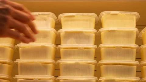 Many plastic containers of butter on a store fridge shelf and a man takes one Stock Footage 196328617