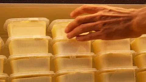 Many plastic containers of butter on a store fridge shelf and a buyer takes one Stock Footage 196552093