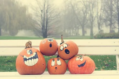 Many pumpinks with painted faces on white porch. Stock Photos