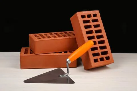 Many red bricks and putty knife on light wooden table against black backgro.. Stock Photos
