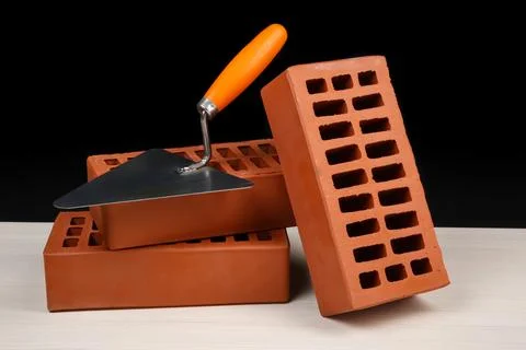 Many red bricks and putty knife on light wooden table against black backgro.. Stock Photos