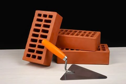 Many red bricks and putty knife on light wooden table against black backgro.. Stock Photos