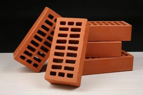 Many red bricks on light wooden table against black background. Building ma.. Stock Photos