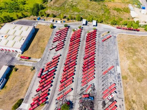 Many red buses are lined up neatly in a large parking area near some building Foto stock
