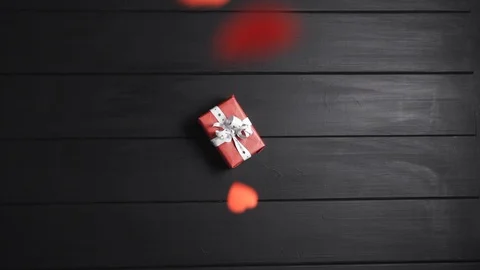 Many red hearts fall on the table, on which lies a box with a gift. Stock Footage 122514746
