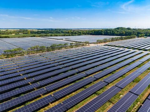 Many rows of solar panels stretch across a flat landscape. Green fields and t Stock Photos
