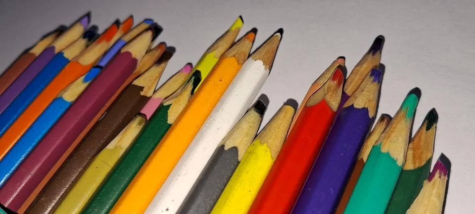 Many sharp colored pencils arranged neatly on a white paper surface Stock Photos