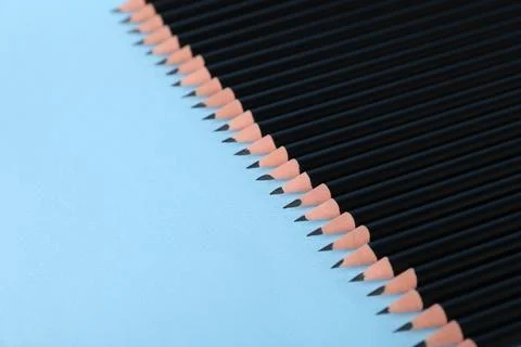 Many sharp graphite pencils on light blue background, closeup. Space for text Foto stock