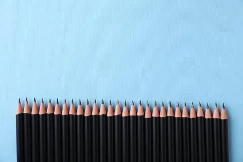 Many sharp graphite pencils on light blue background, flat lay. Space for tex 写真素材