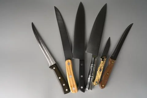 Many sharp knives of different sizes on a gray background. Stock Photos