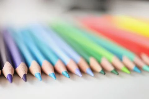 Many sharp multicolored pencils lying over colors of rainbow closeup background Foto stock
