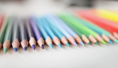 Many sharp multicolored pencils lying over colors of rainbow closeup background Stock Photos