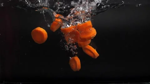 Many slices of fresh carrots fall into the water with spray, slowly sinking to t Stock Footage 133354702
