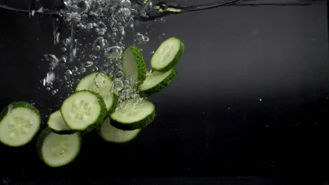 Many slices of green cucumber fall into the water with spray, slowly sinking to Stock Footage 133354464