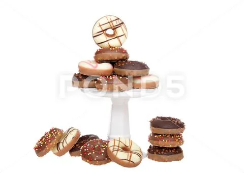 Many small donuts coated in candy and decorated with sprinkles stacked on a s Stock Photos