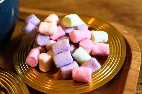 Many small multi-colored marshmallows on a golden plate. Stock Photos