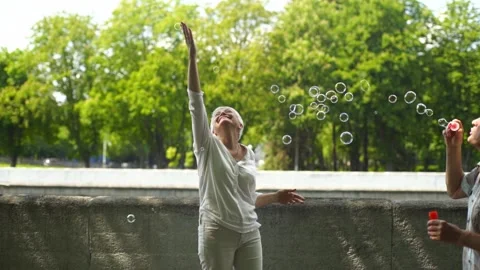 Many soap bubbles surround a happy elderly woman in white on a sunny summer day Stock Footage 198720890