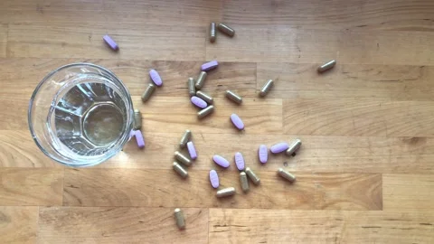 Many tablets and capsules on the table with a glass of water. Top view Stock Footage 228952571