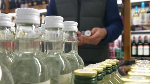 Many vodka bottles in alcohol store and a man with a shopping trolley takes one Stock Footage 336358518