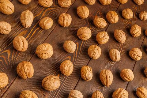 Many walnuts with shells evenly spread out on brown wooden surface Stock Photos