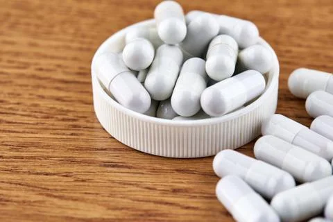 Many white capsules in plastic cap on wooden background Stock Photos