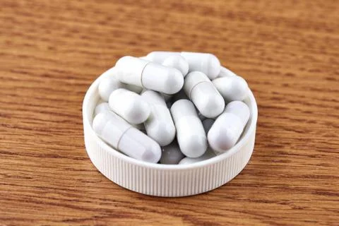 Many white capsules in plastic cap on wooden background Foto stock