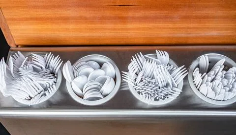 Many white disposable plastic spoons, forks and knifes at cafeteria. Fast-f.. Stock Photos