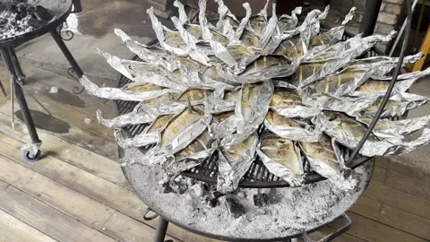 Many white fish cooked on round stand with fire in silver paper. Stock Footage 245339974