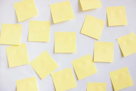 Many yellow papers for notes on a white wall. Stock Photos
