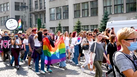 Many young people with rainbow flags and rainbow masks walk through the city Stock Footage 211882425