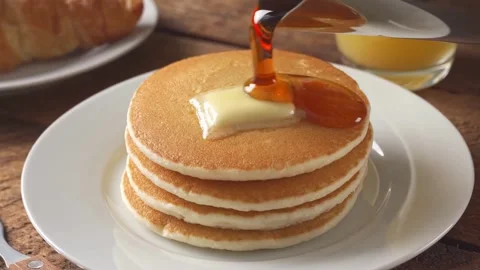 Maple syrup being poured on stack of steaming buttered pancakes. Stock-Footage 336589017