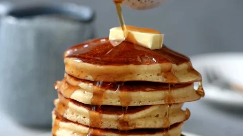 Maple syrup being poured on stack of steaming buttered pancakes. Stock-Footage 336589041